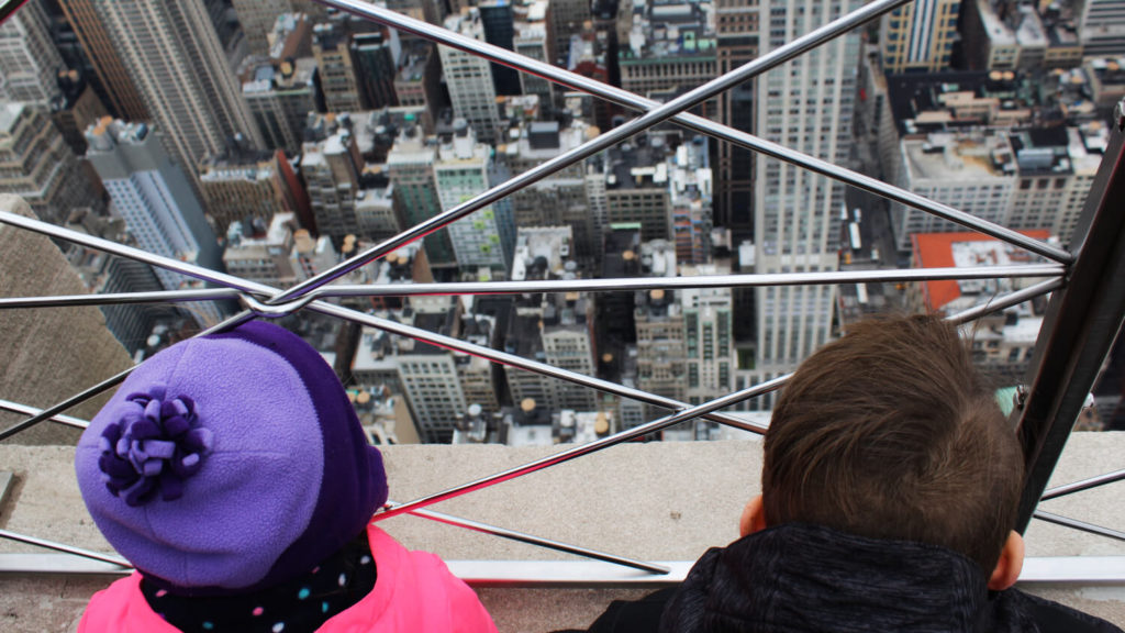 two children look down below at New York City from the top of the empire state building