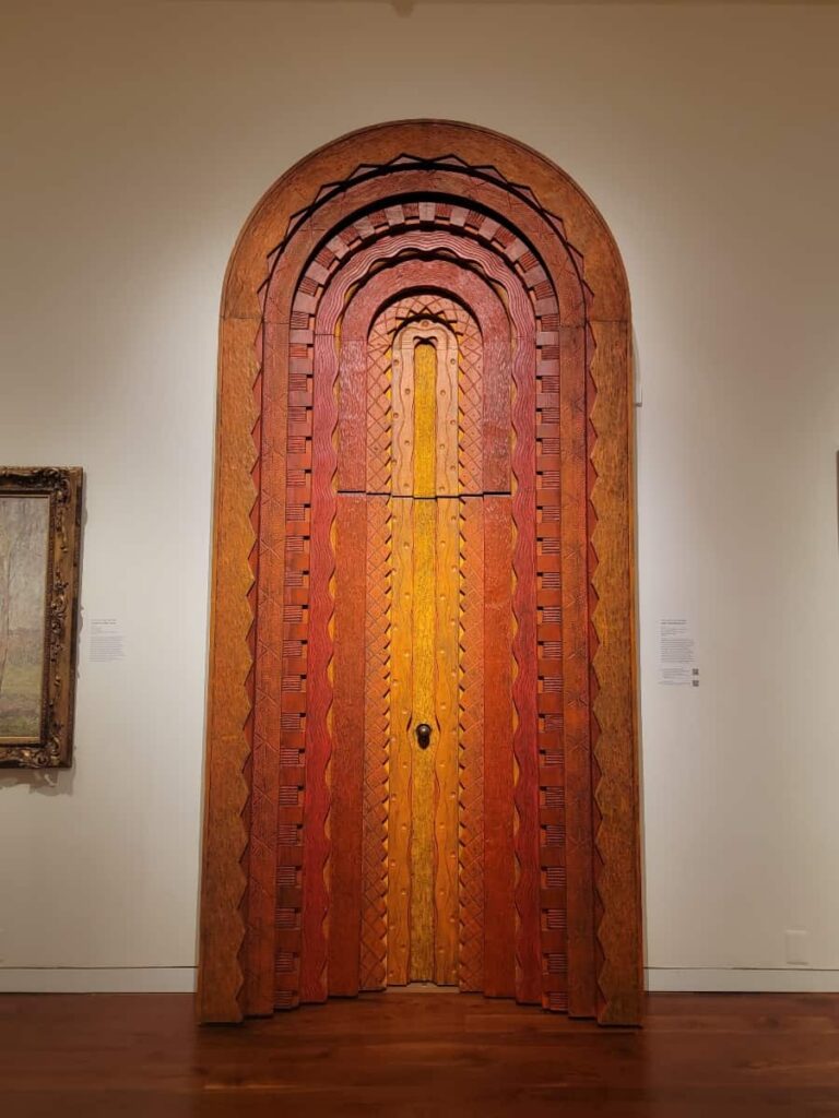 A large carved wooden door with an arched top is red, yellow, and orange