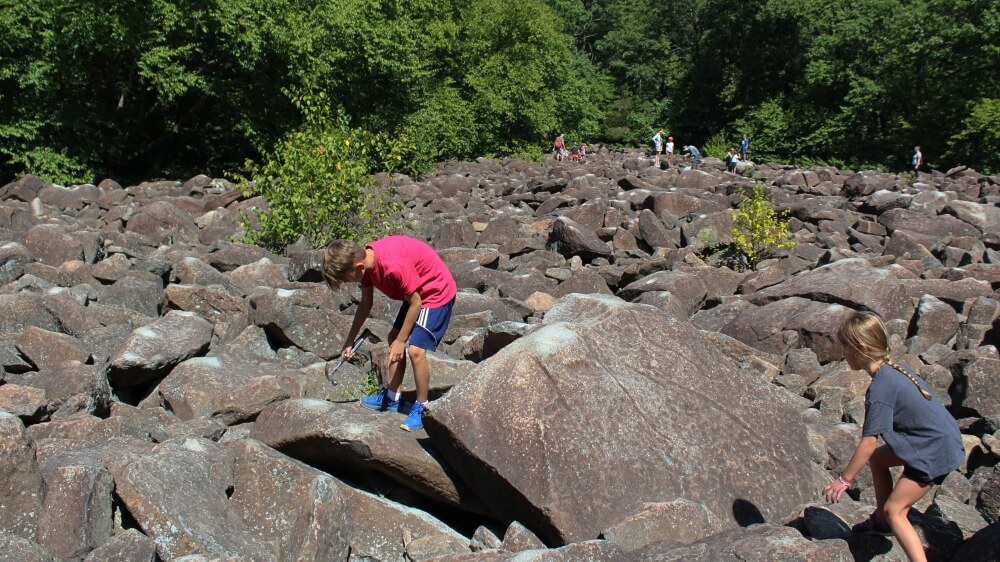Family-Friendly hikes near Philadelphia  - Boy and girl banging on large boulder with hammers at Ringing Rocks County Park