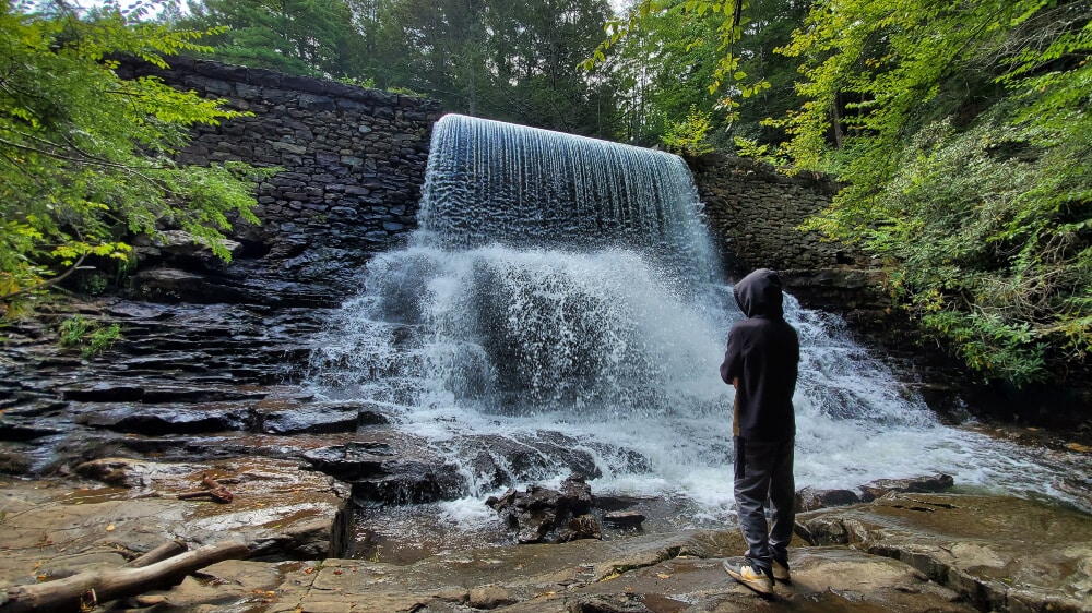 boy stands in front of man made water fall on the shades of death trail in hickory run state park