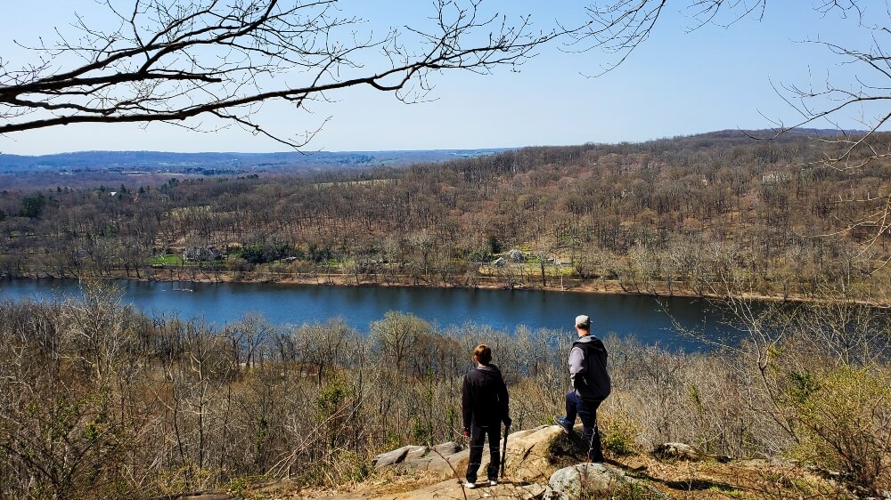 father and son standing with a view of Bucks County in Pennsylvania and the Delaware River from the Goat Hill Overlook trail in Lambertville, New Jersey. One of the best family-friendly hikes near Philadelphia