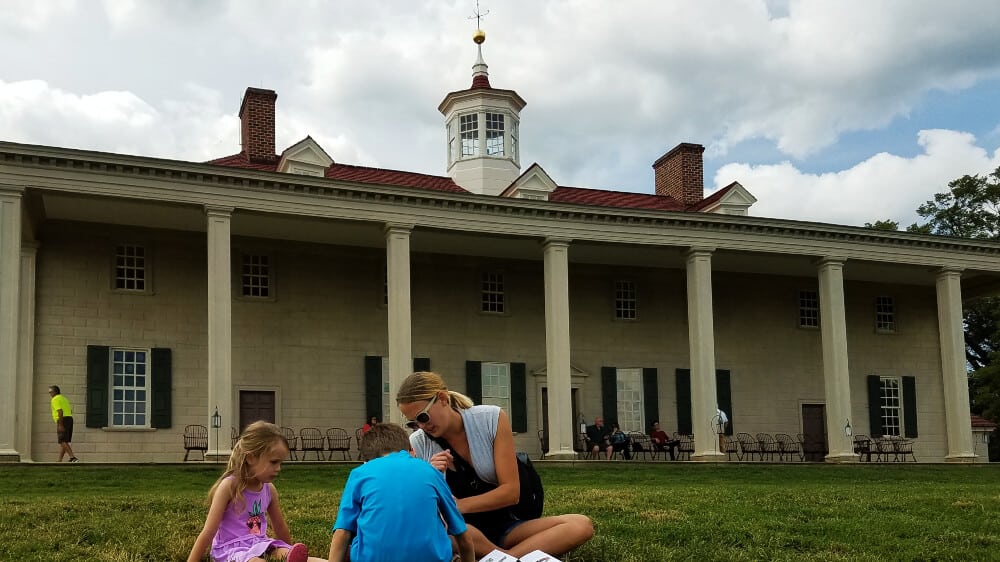 Family sitting on lawn next to George Washington's Mount Vernon mansion