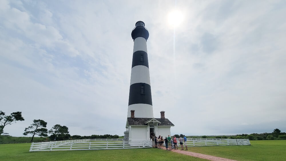 The Bodie Island Lighthouse stands as a group of people walk in at the base