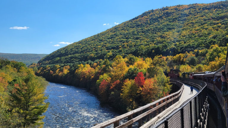 a train rolls along on a track next to the lehigh river in early fall