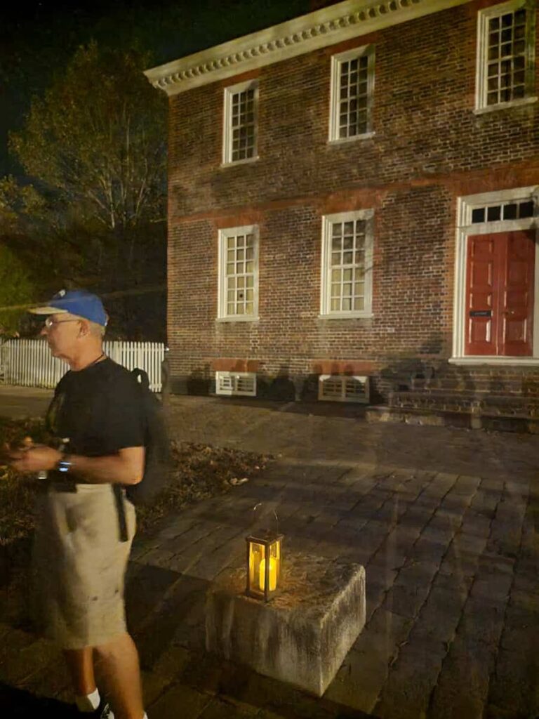 a man stands in front of a colonial building with a lantern during a ghost tour in williamsburg