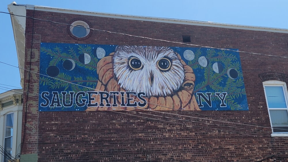 A mural painted on a brick building shows an owl with the town name "Saugerties" written across