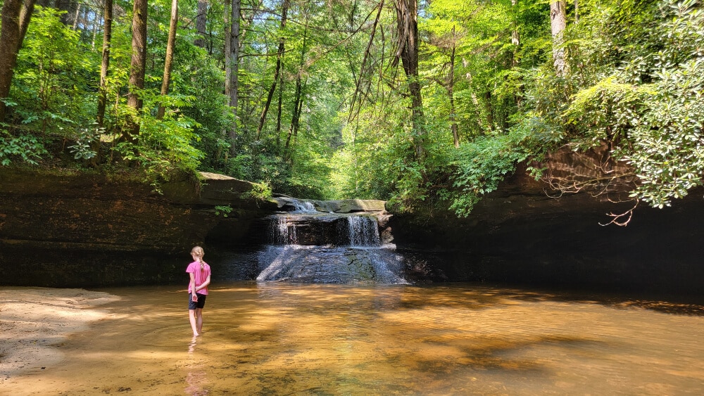 best things to do in red river gorge - a young girl wades through the water at the base of creation falls waterfall