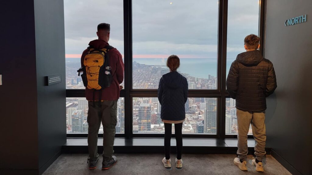 Three people looking out the north window at the Willis Tower Skydeck 