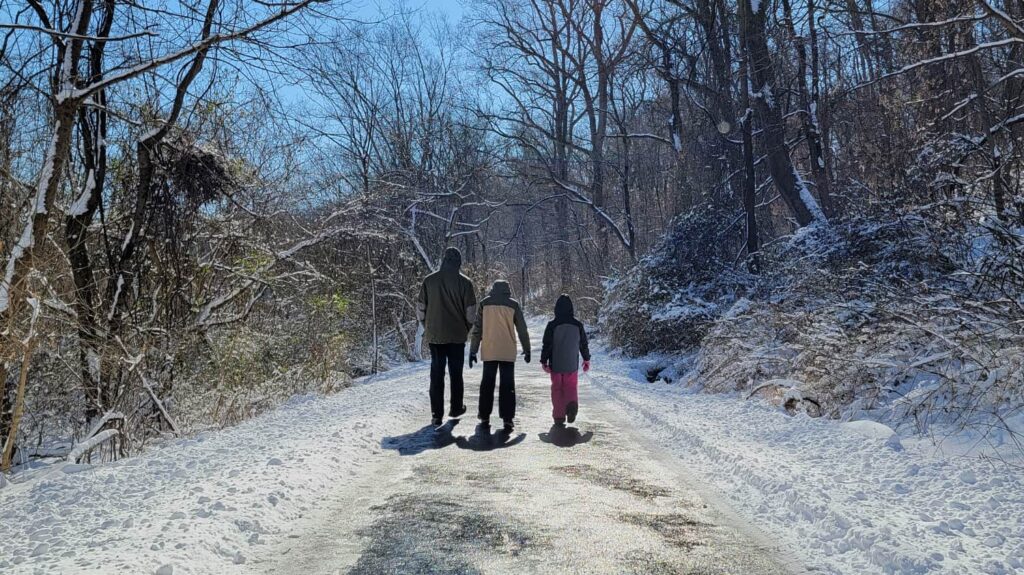 a family walks along a snowy path with the sun shining. Moving helps keep you warm when its cold outside.