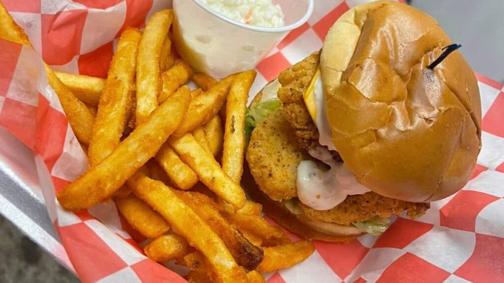 a fried frish sandwich with a cream sauce sits on red and white checked paper with fries