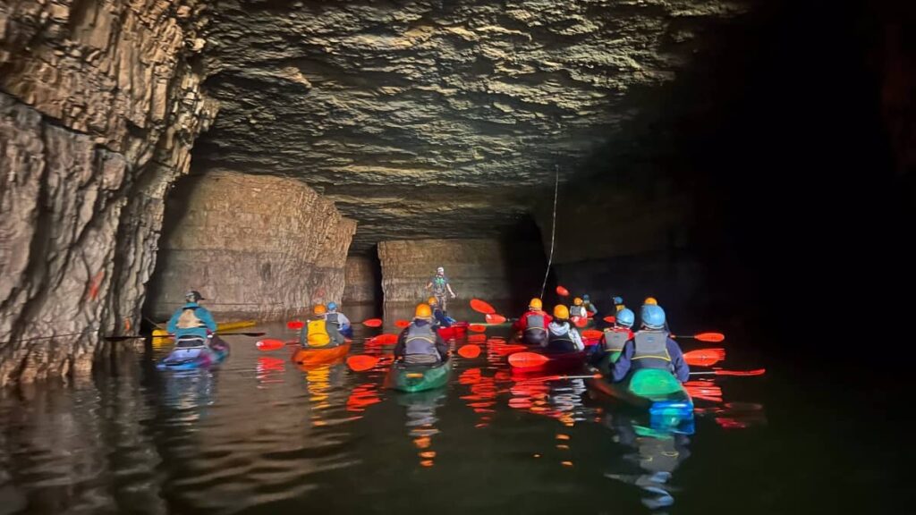 a group of people sit in kayaks while touring a cave in Red River Gorge