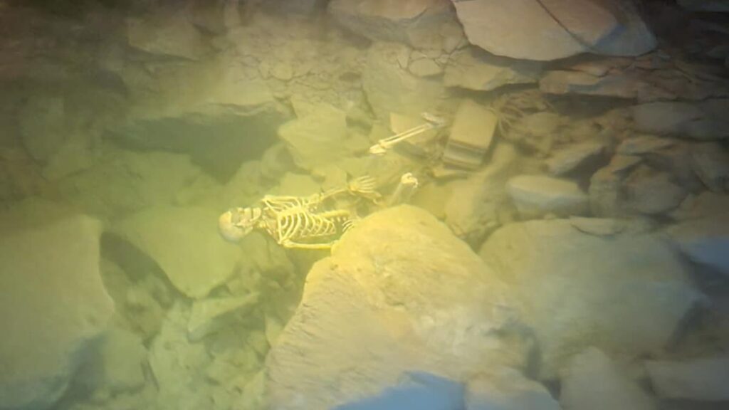 a fake skeleton is seen at the bottom of the cave floor