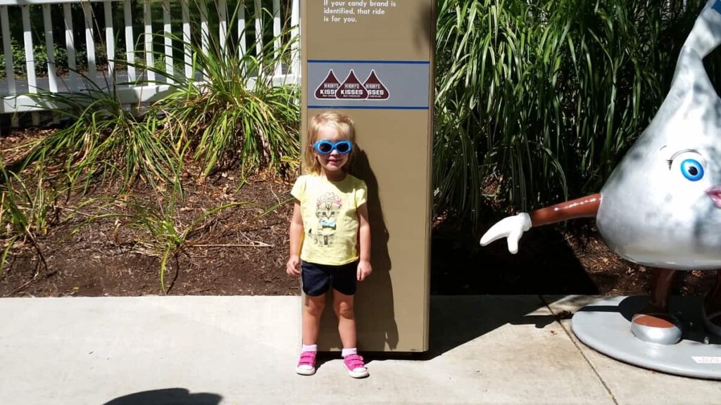 Little girl stands in front of Hershey Kiss measuring post and is is just slightly too short.