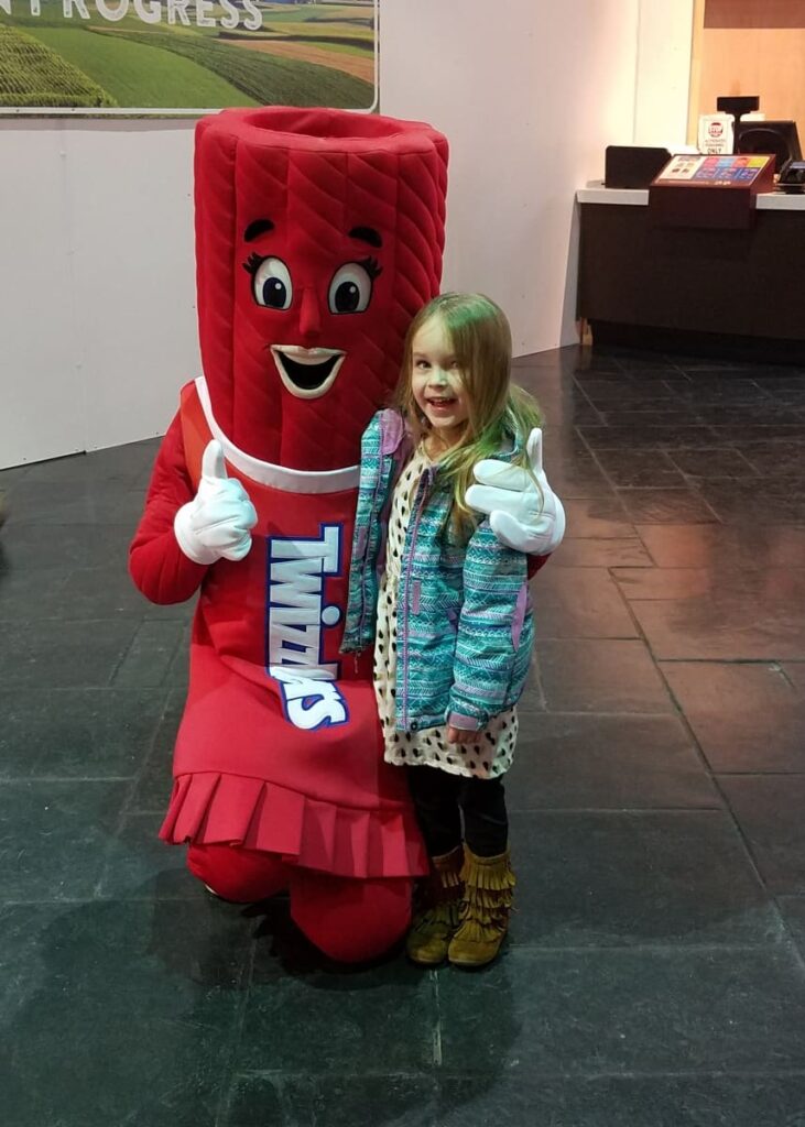 Little girl stands with a Hershey character made to look like Twizzlers
