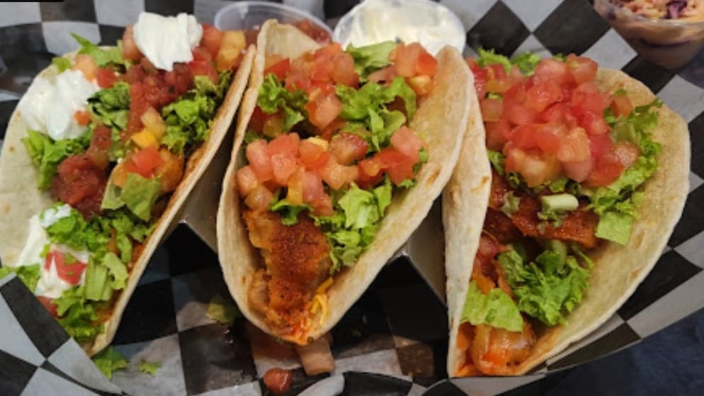 three fish tacos are aligned in a basket with black and white checkered paper