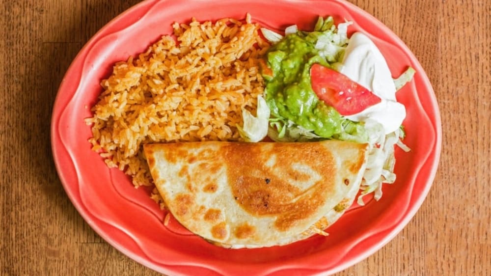 a quesadilla, rice and guacamole sit on a red plate 