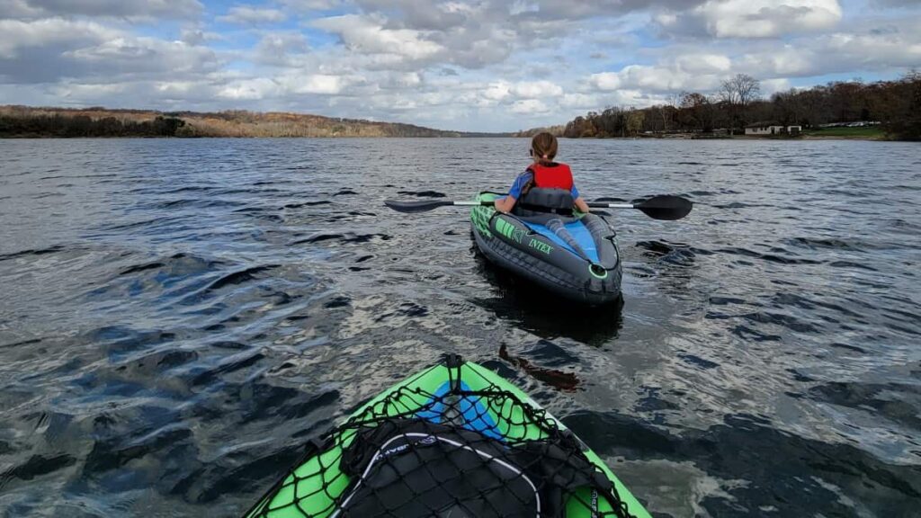 a young girl is seen kayaking in front of another boat on a large lake