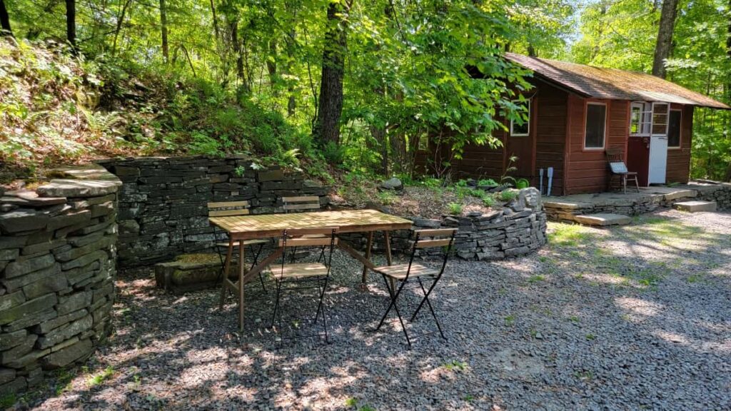 a small wooden tables with folding chairs sits on crushed rock under the shade of trees