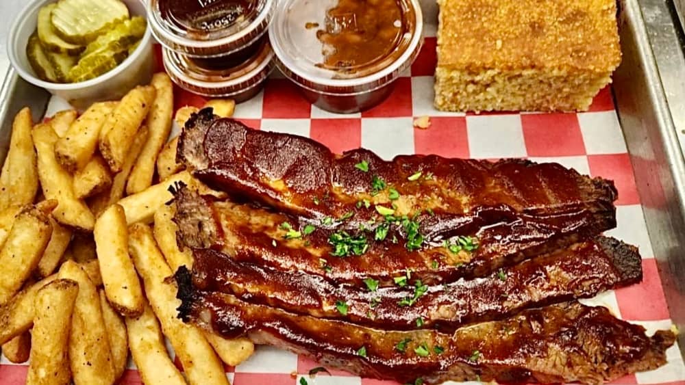 barbecue ribs and fries sit on a red and white checkered napkin