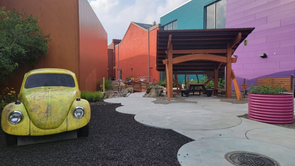 A yellow VW bug sits in the outdoor play yard at a children's museum in Erie