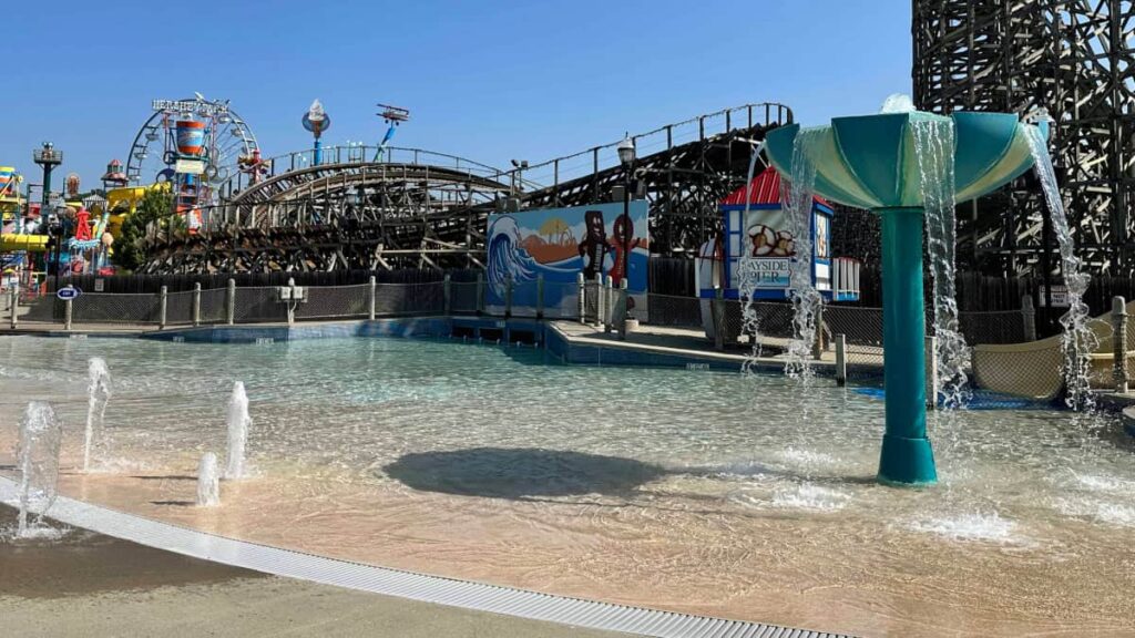 a zero entry water area with sprayers and fountains and roller coaster in the background