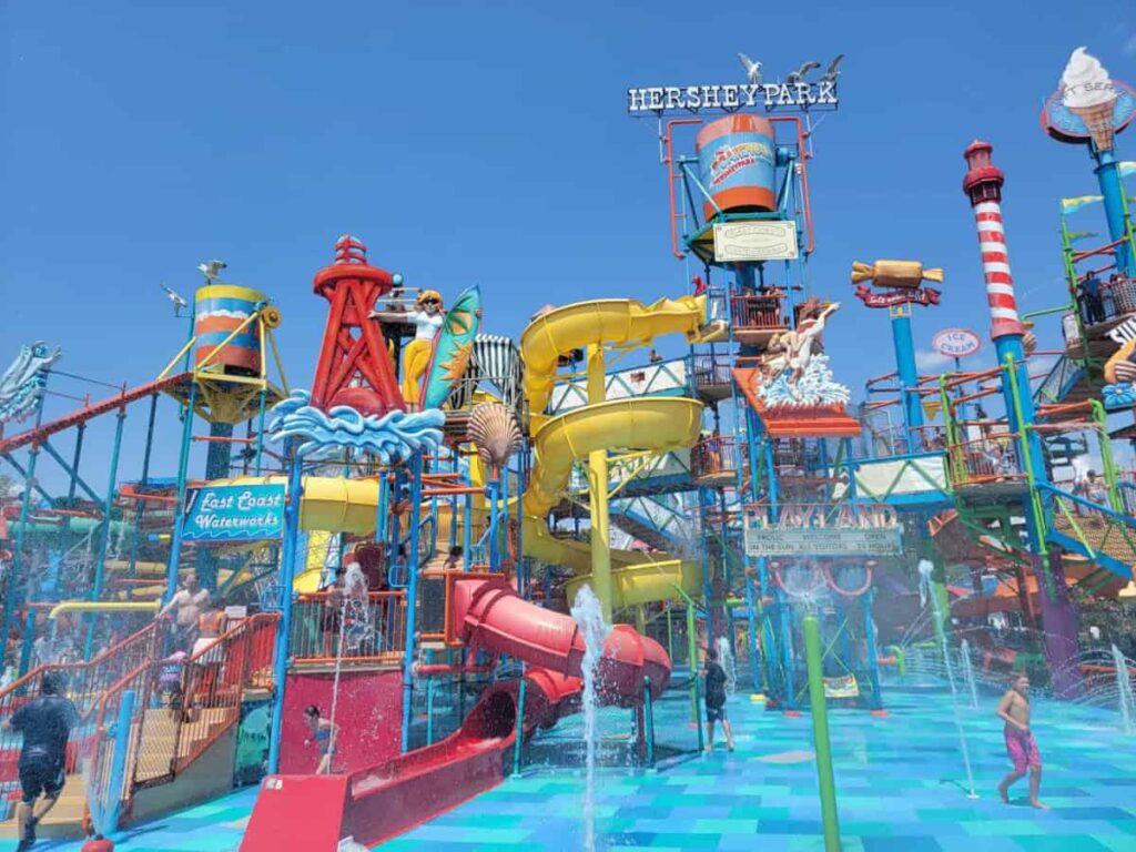 Parents and kids play on a large water play structure with dumping bucket and slides