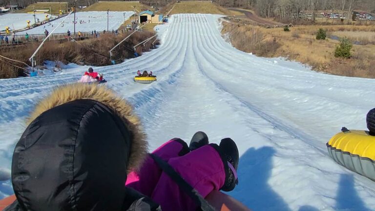 a young girl sits at the top of a mountain waiting her turn to snow tube