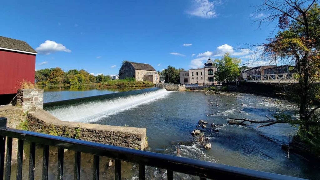 A river with a short dam with a red building and stone building on opposite sides