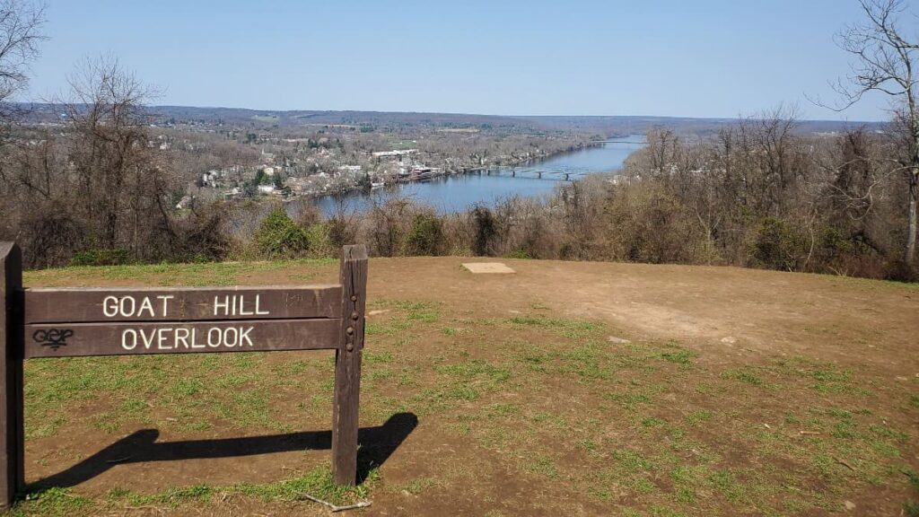 a wooden sign reads "goat hill overlook" with the Delaware River and New Hope Lambertville bridge in the background