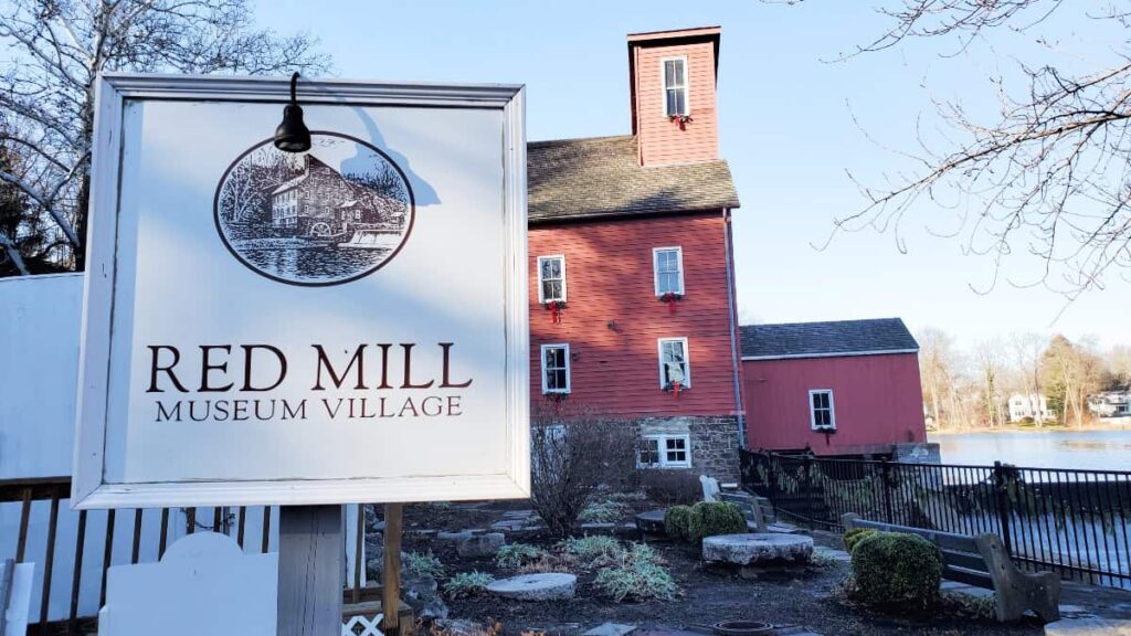 a sign reads "red mill museum village" with a red building behind