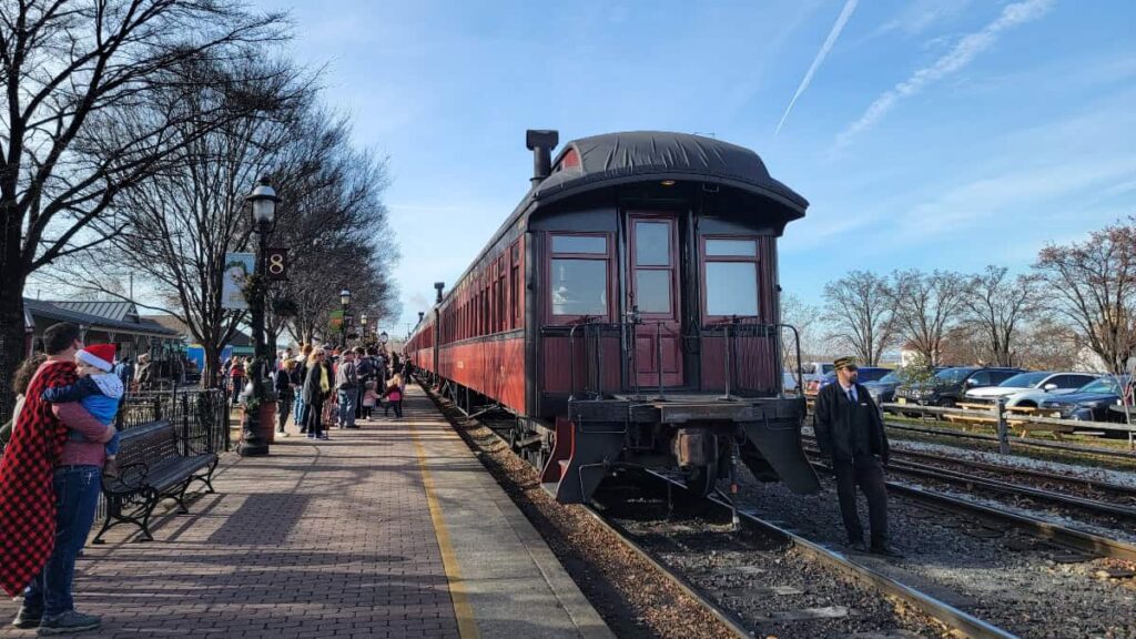 people stand on a train platform waiting to board the strasburg railroad holiday train