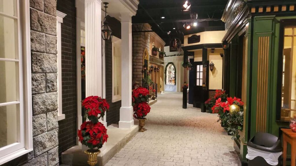 A walkway looks like a Victorian England street with building facades decorated for Christmas