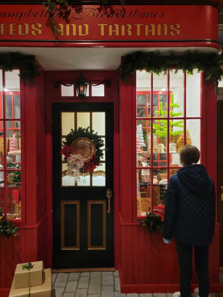 a young girl looks in a window of a toy store facade at Byers Choice