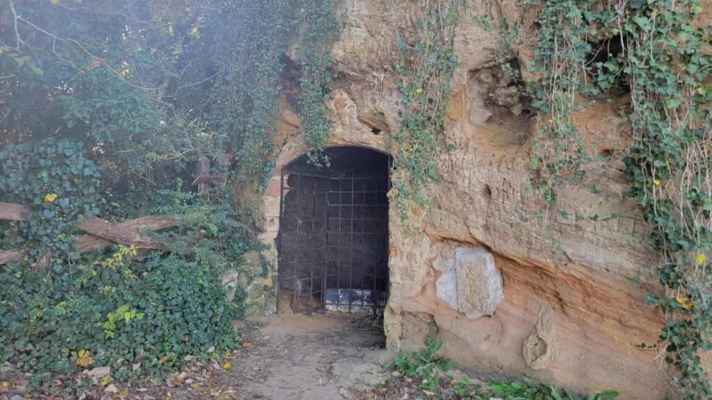 View of the entrance to a small cave. the entrance is blocked off by an iron fenced door