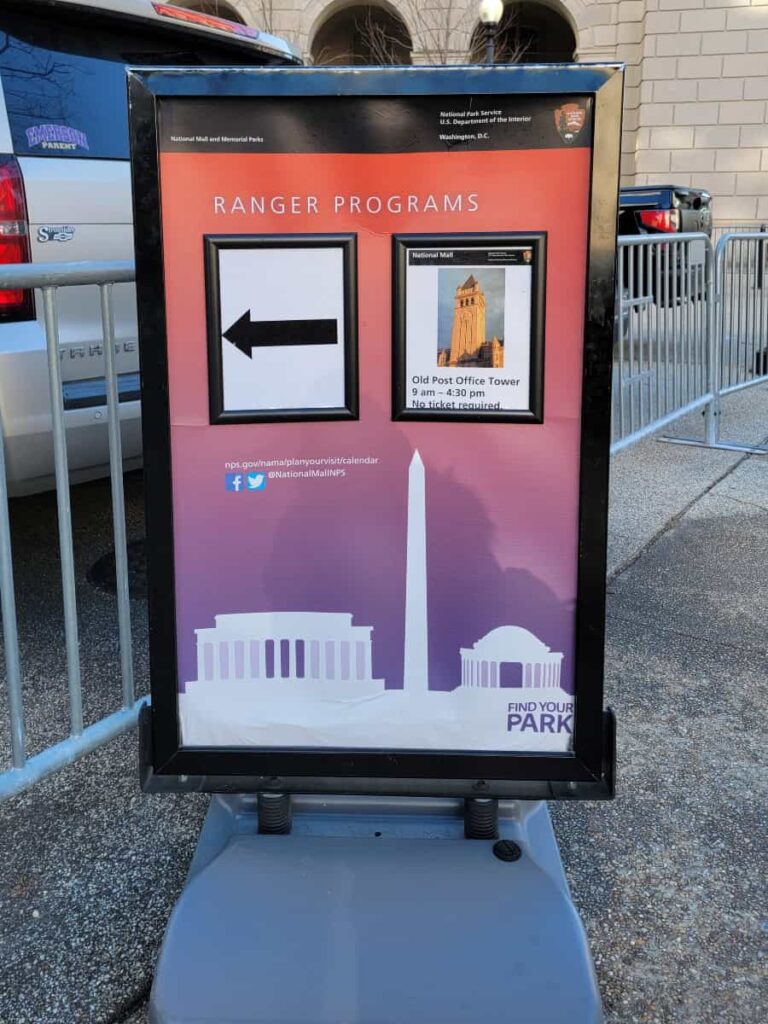 A sign on the sidewalk indicates the entrance for the Old Post Office Tower and Museum