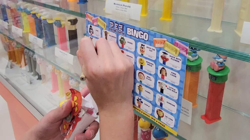 A child leans against the glass of a PEZ dispenser display case to check boxes off a scavenger hunt list